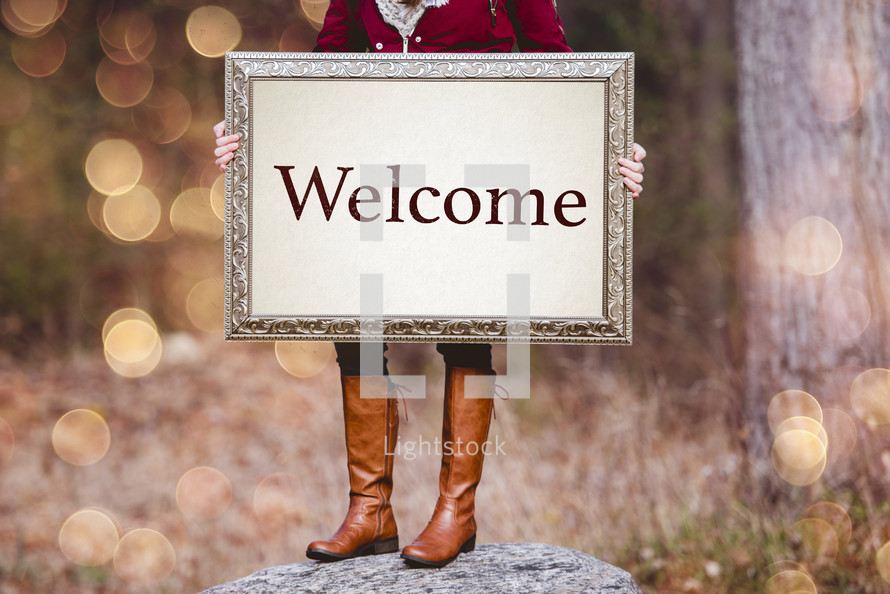woman holding a canvas sign that reads welcome 