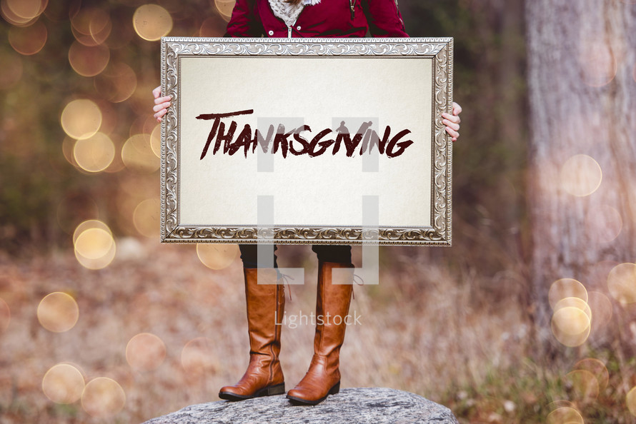 a woman holding a sign the reads thanksgiving 