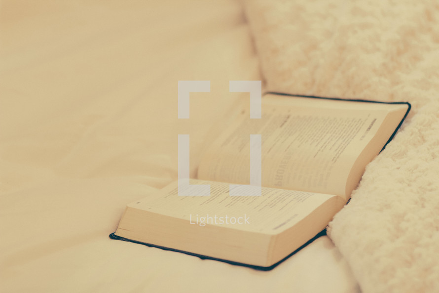 An open Bible laying on a bed.