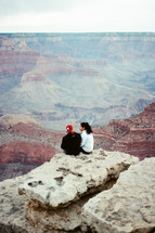 couple sitting on a cliff looking out at the grand canyon 