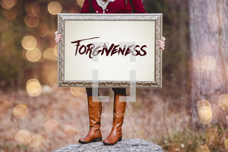a woman holding a sign the reads forgiveness 
