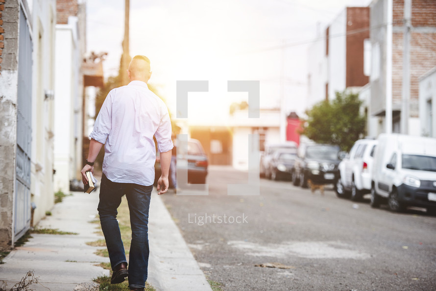 man walking down a sidewalk carrying a Bible 