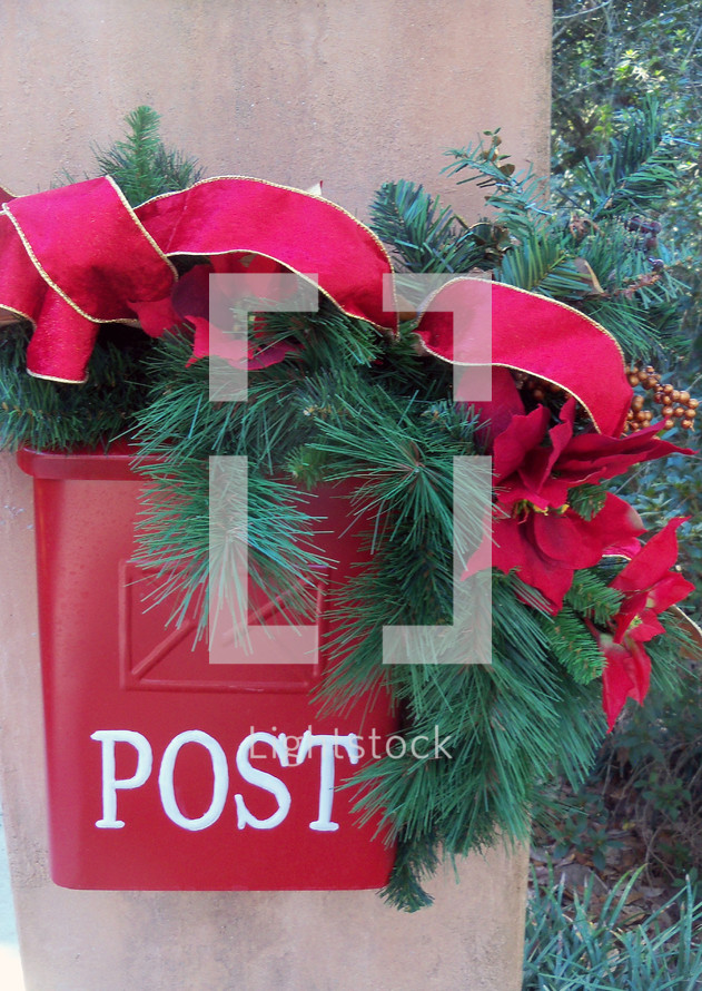 A red postal box mail box with the words POST is decorated with green branches, red flowers and red ribbons to celebrate Christmas and bring some Christmas cheer.