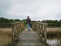 man crossing over a footbridge over a marsh 