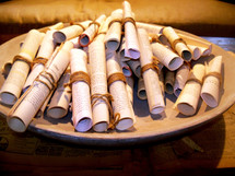 A bowl filled with old rolled up paper manuscript scrolls with the word of God and bible lessons printed to give out to people. In the early days, the word of God was written on parchments of scrolls of linen paper such as papyrus dating as far back as the early church. These scrolls are a reminder of how the word has endured the test of time and that the word of God is timeless enduring forever and a reminder that God's word will not return unto Him void but accomplish that which He pleases. Which is why we need to share the word of God as often as we can to tell people about Jesus.  