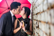 a couple kissing under a red umbrella 