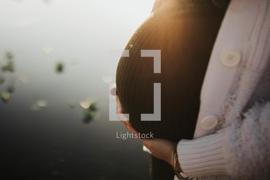 a pregnant silhouette against a sun setting on the lake 