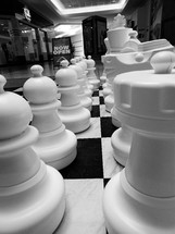 A black and white image of a huge chess board with chess pieces in black and white on a checkered black and white chess board that takes up about 10 feet of floor space symbolizing the game of life, life and death, good and evil, risk and chance and strategy and planning. All the things that make up life and thinking through moves that we make that can affect our spiritual and physical as well as mental well being. 

I saw this huge chess board at a local shopping mall and it just captured my imagination and had to photograph it. 