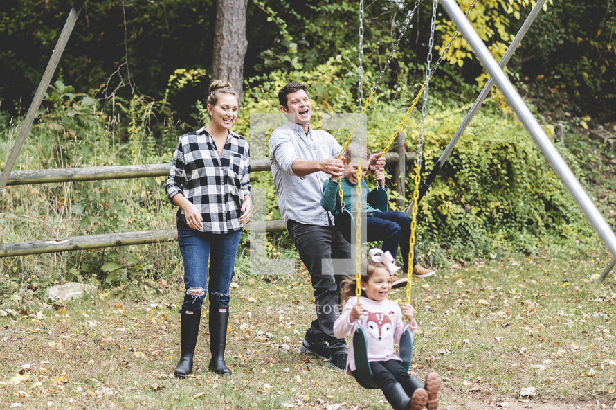 family playing outdoors on a swing set in the backyard in fall
