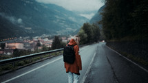 a woman in rain gear backpacking down a road 