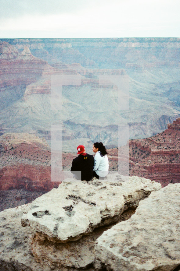 couple sitting on a cliff looking out at the grand canyon 