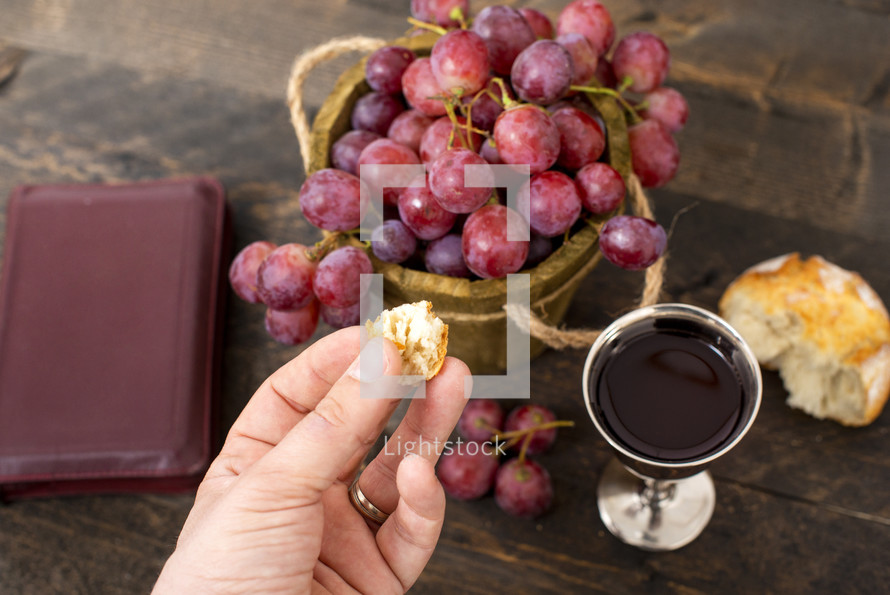 Man breaking the bread, with wine, grapes and Bible in the background