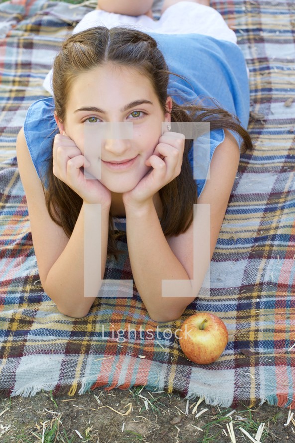 a smiling teen girl lying on a plaid blanket 