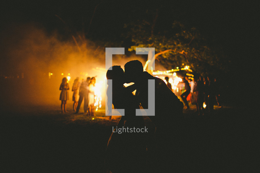 Silhouette of couple kissing by a campfire.
