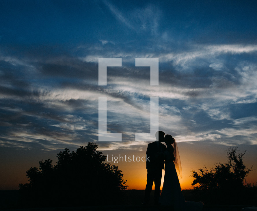 Silhouette of a bride and groom kissing at sunset.