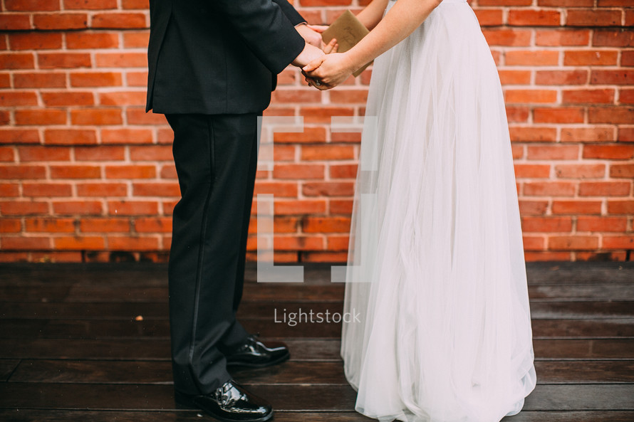 Bride and groom holding hands outside in front o a brick wall.
