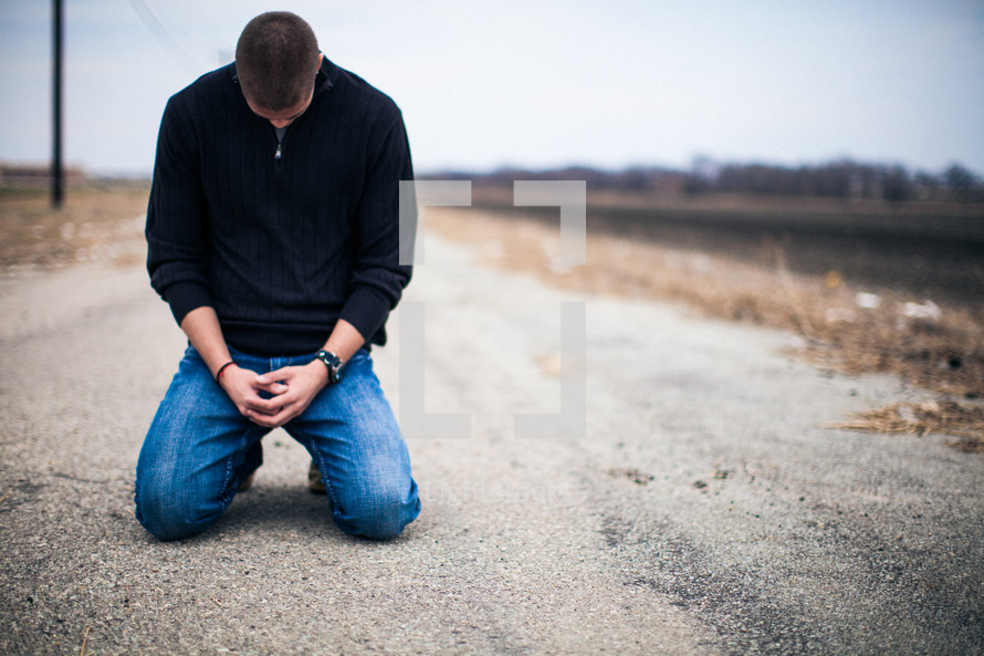 man kneeling on a road praying