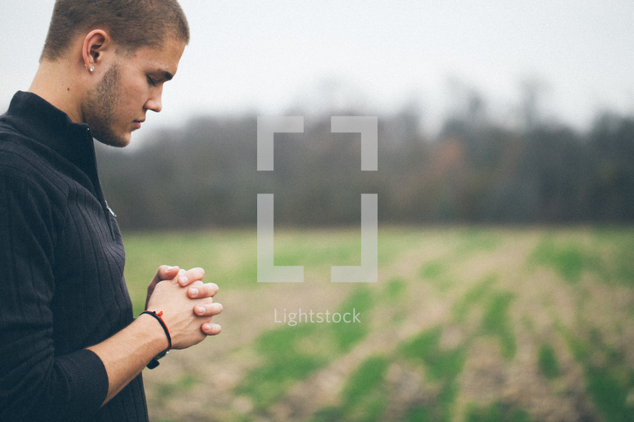 man standing in a field with his head bowed in prayer