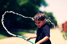 A young boy playing with a water hose 