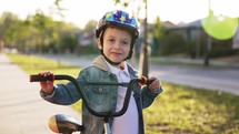 Happy smiling boy in helmet riding a cycling. Little boy learns to ride a bike in the park near the home. Sport activity for children. Child development concept.