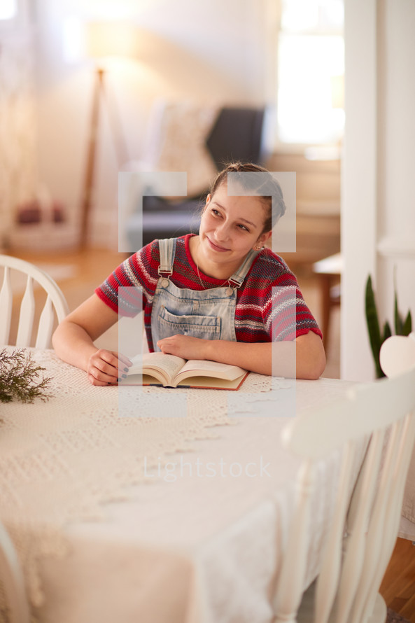 girl reading a Book at a kitchen table looking away