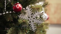 Slow-motion footage of a snowflake Christmas ornament on an ever-green tree during the winter holidays.