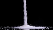 Pouring white sugar on black background in slow motion. The benefits or the danger of sugar consumption to health concept.
