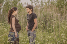 Expecting couple standing in a field of tall grass.