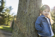 toddler girl leaning against a tree 