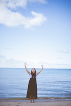 woman with hands raised praising God on a beach 