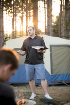 man reading a Bible around a campfire 