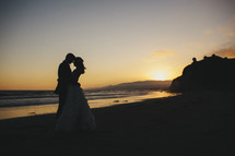 bride and groom standing on a beach at sunset