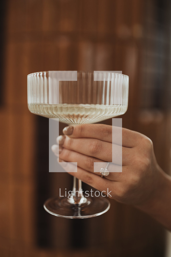 Hand holding a champagne glass with engagement ring