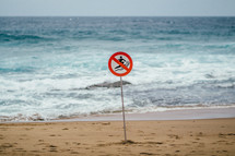 A sign on the beach by the ocean denoting that it is a no surfing area.
