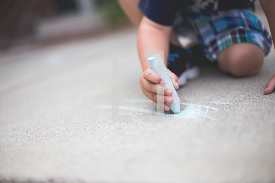 Little boy drawing on the sidewalk with chalk.