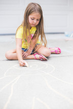 A young girl drawing on the floor with chalk.