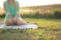 a young woman sitting on a blanket in the grass 
