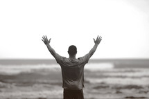 man standing in front of the ocean with raised hands 