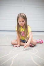 A young girl drawing on the driveway with chalk.
