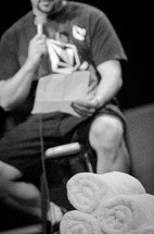 Man sitting on a stool on a stage reading notes into a microphone.
Baptism
