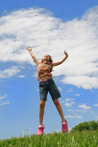 young girl jumping up in the air on a hillside