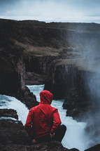 a man in a red coat standing in front of a waterfall 