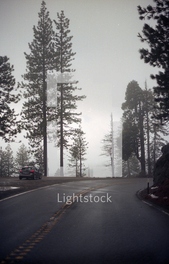 car parked on the side of a mountain road on a foggy morning 