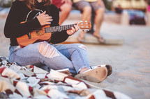 girl playing a ukulele on a beach 
