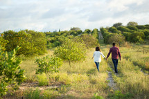 a couple holding hands walking in an orchard 
