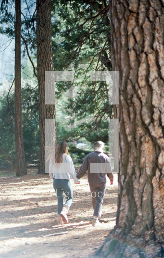 a couple walking holding hands in the woods 
