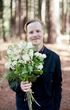 a man holding a bouquet of flowers in the woods 