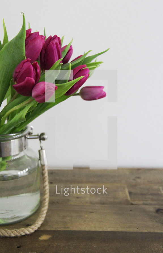 Purple tulips in a vase on a wooden table.
