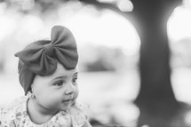 an infant girl in a headband with a bow outdoors 