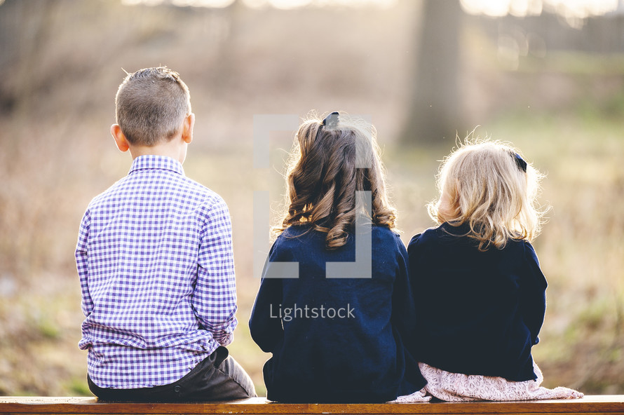 kids sitting on a bench with backs to the camera 